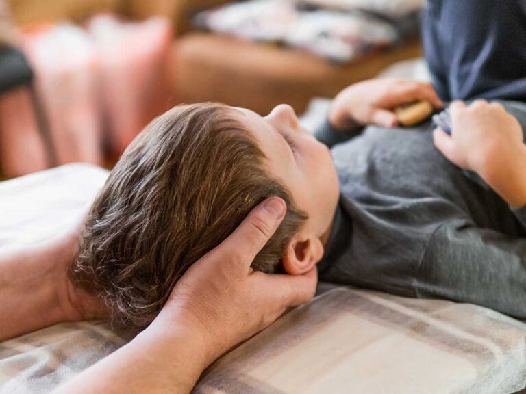 A person sitting on a couch applying an ice pack to their lower back in a cozy, lived-in home.