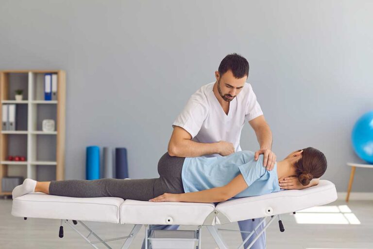 Older adult performs gentle mobility exercises beside a treatment table with guidance from a clinician.