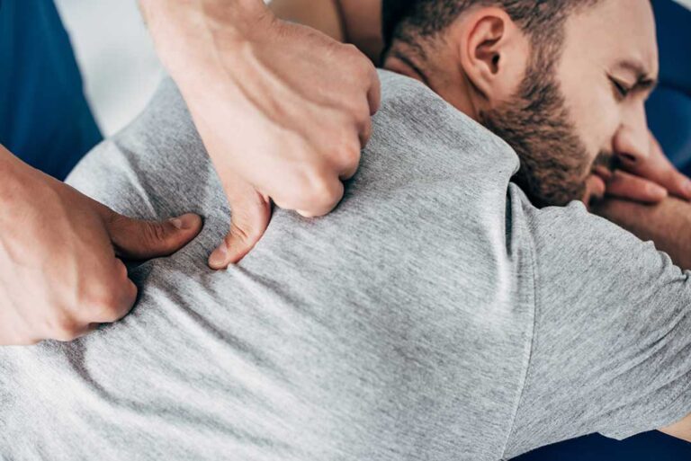 A person gently stretching their back while standing in a sunlit living room.